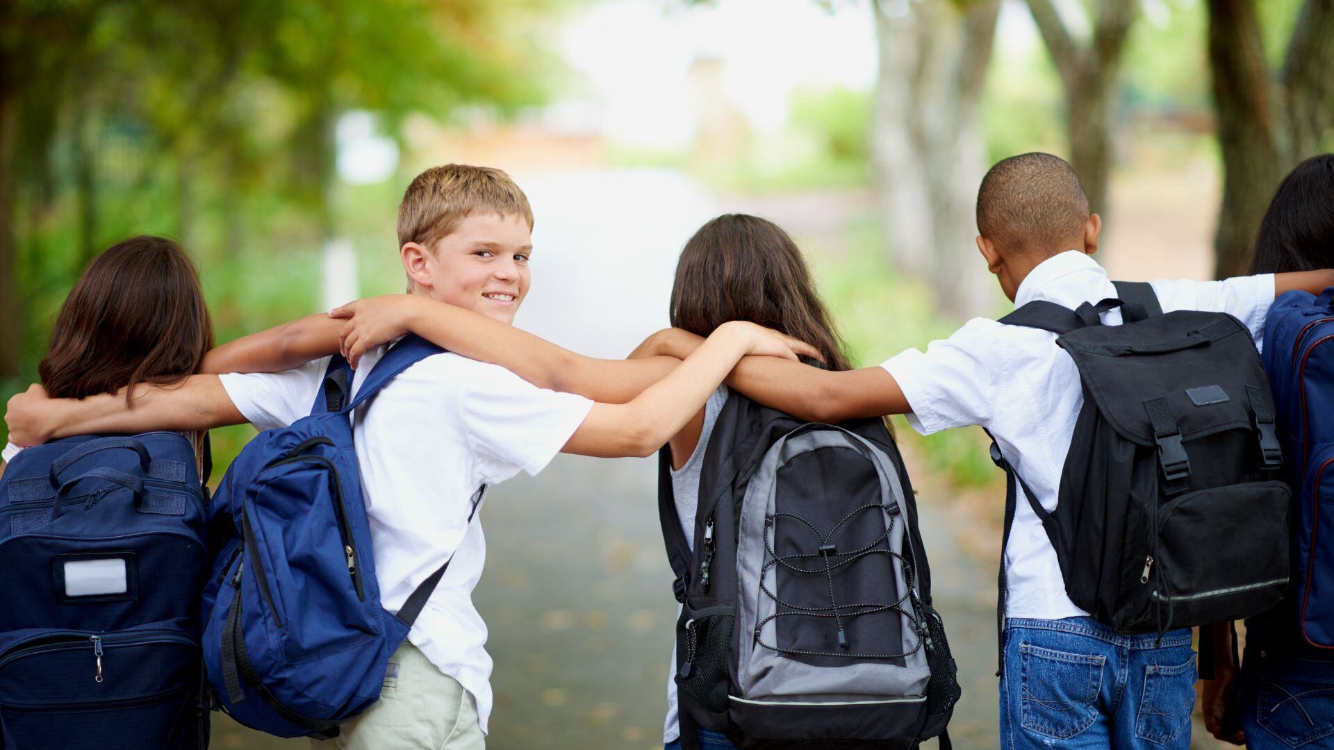 kids carrying backpacks walking along a path together